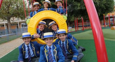 Group of school children wearing straw hats pose a playground equipment