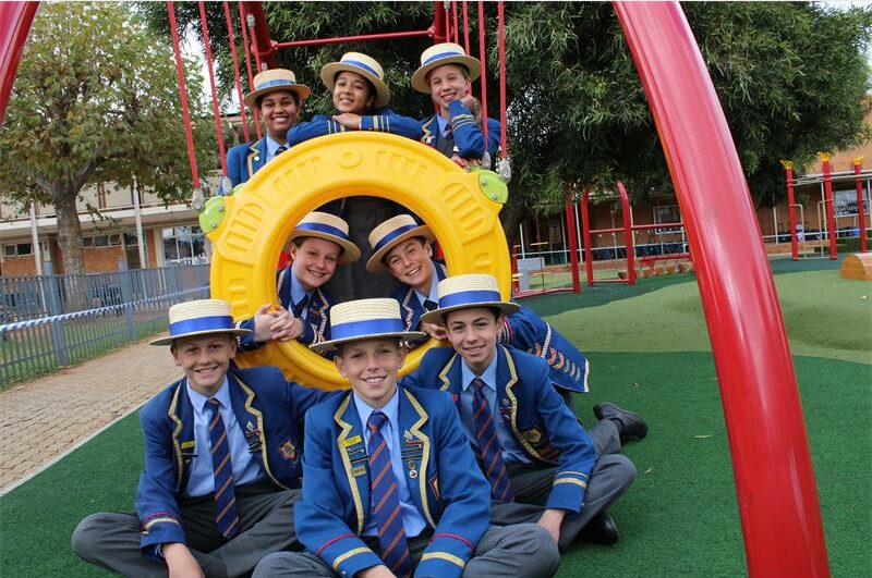 Group of school children wearing straw hats pose a playground equipment