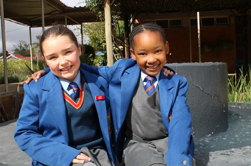 A white girl and black girl in school uniforms with their arms around each other