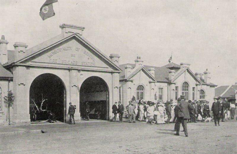 A black and white photo depicting an old building with two big doors open that housed a fire station.
