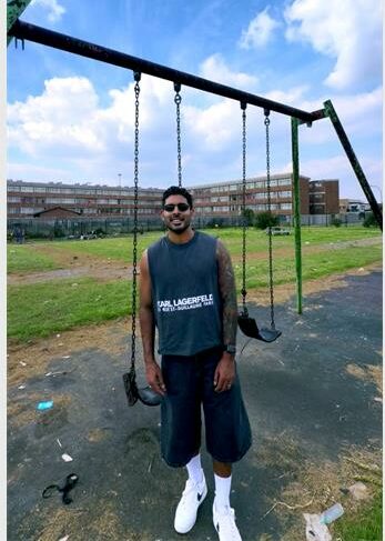Indian man standing at a swing set with flats in the back ground