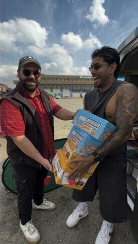 Man with a red shirt hands an Indian man a stack of boxes