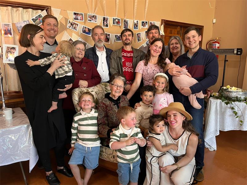 Groep mense staan om 'n bejaarde vrou