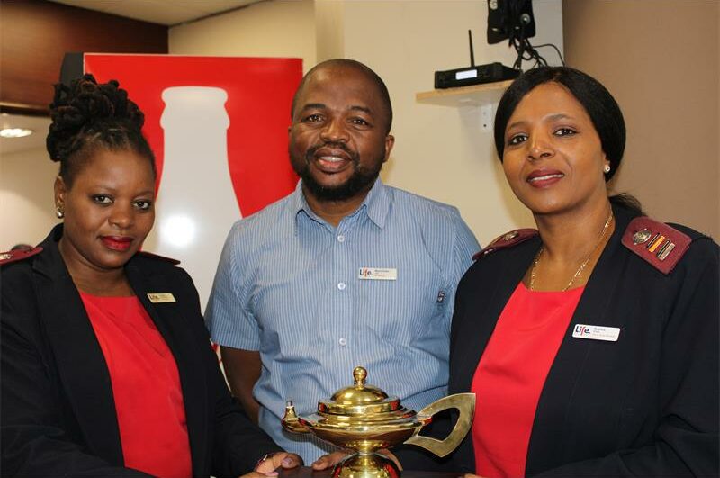 Two black women in uniform and one black man holding a bronze lamp