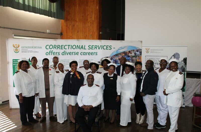 Group of nurses wearing white uniforms standing in front of a Correctional Services banner