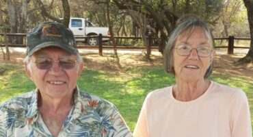 An elderly man and woman, him wearing a cap and she glasses.