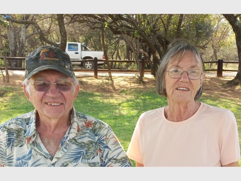 An elderly man and woman, him wearing a cap and she glasses.
