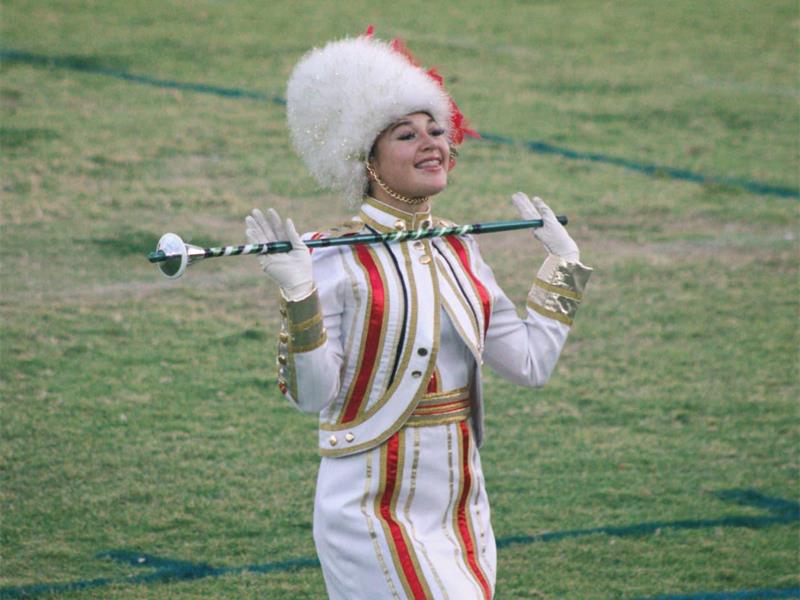 A girl in white and red majorette uniform holding a stick