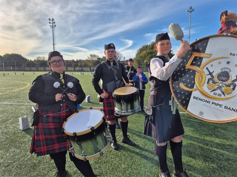 Four members of a pipe band performing on various instruments.