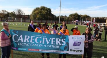 Community group holding "Caregivers Facing Cancer Together" banner at outdoor event in Benoni.