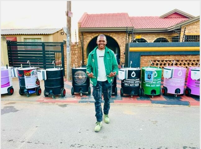 A guy standing in front of colourful hand washing stations.