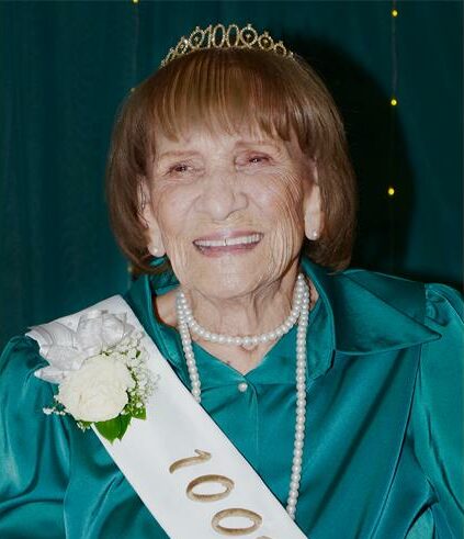 Elderly woman wearing a tiara and a sash with the number 100 in gold