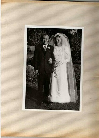 A black and white photograph of a man and woman on their wedding day, taken in a garden.