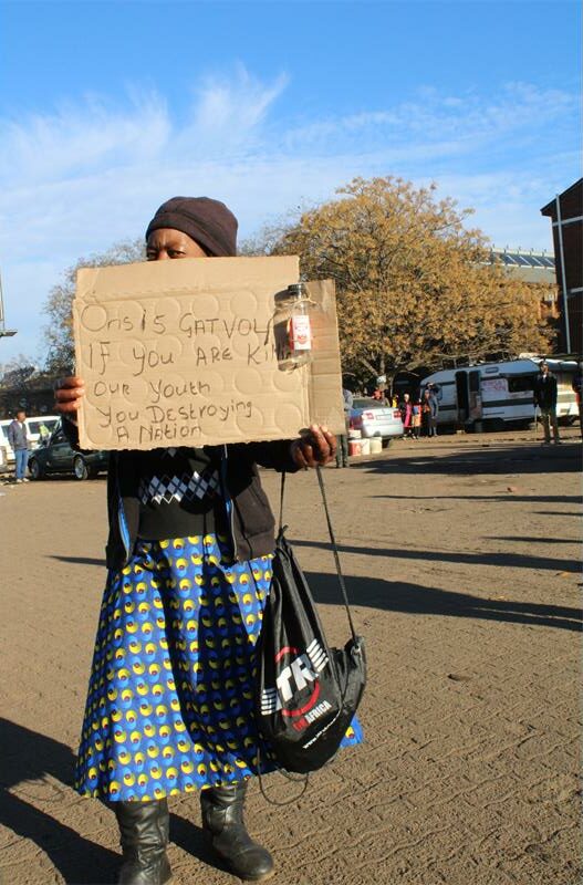 Black woman holding a hand written poster in front of her face