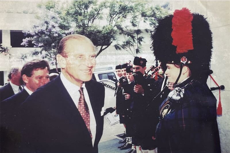 Grainy photo of Prince Phillip passing pipe band members and the drum major wearing a busby