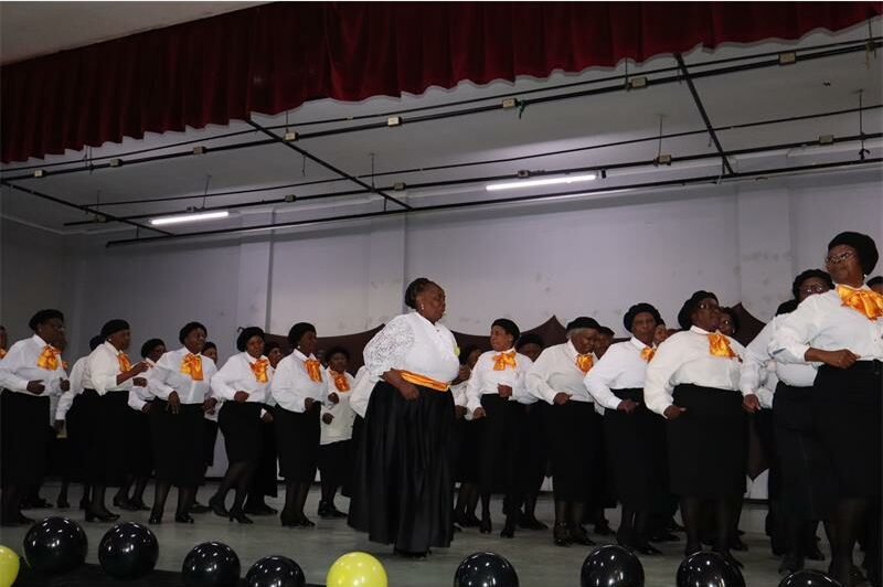 Group of black women wearing black skirts, white shirts and yellow scarfs