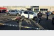 A parking area crime scene with two vehicles and suspects on the ground and a police officer in view.
