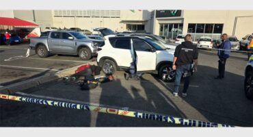 A parking area crime scene with two vehicles and suspects on the ground and a police officer in view.