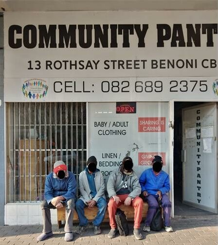 Four men, with their faces blocked out, sitting in front of a store front