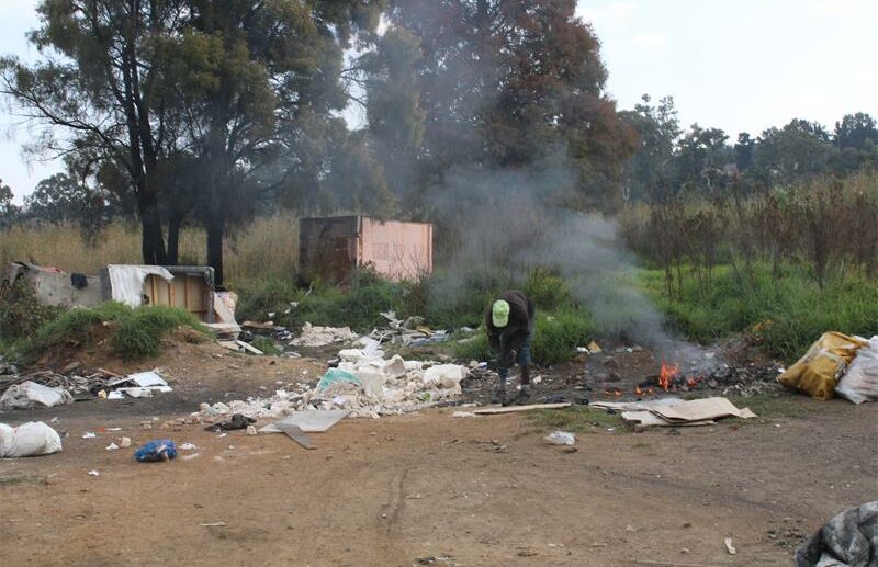 Man stands bent over scratching among rubbish with a fire burning