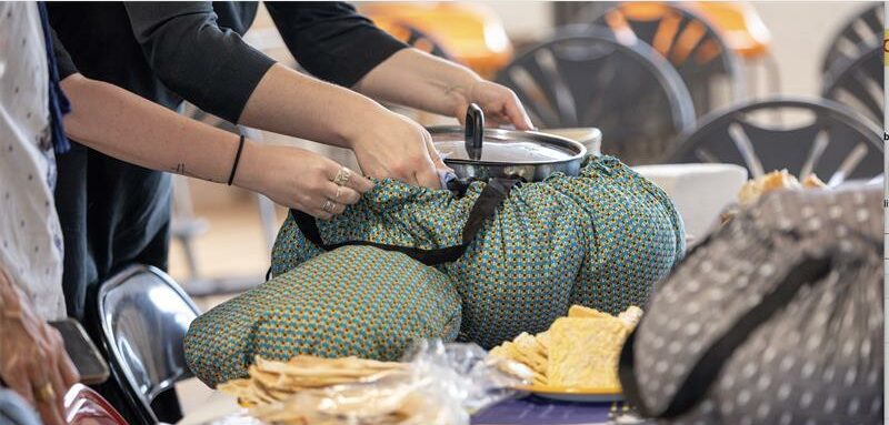 A wonderbag slow cooker on a table with a view of hands tying the cooker cosed.