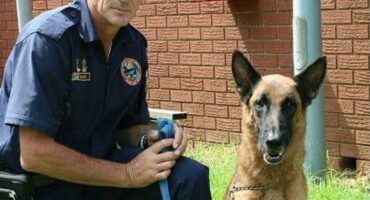 Man in a police uniform kneeling next to a dog