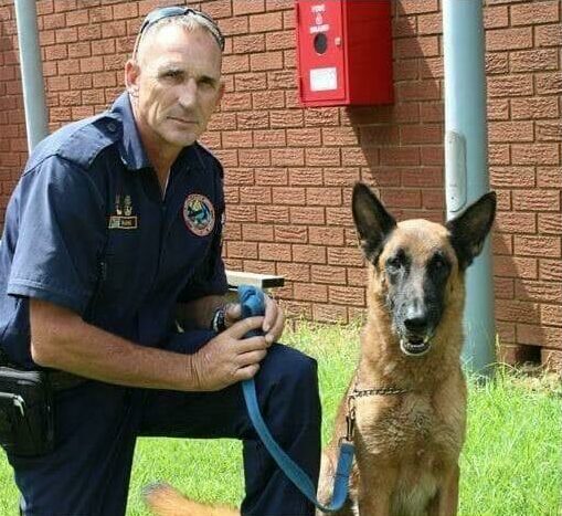 Man in a police uniform kneeling next to a dog