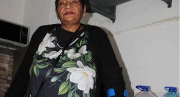 Indian woman balances on a crutch standing next to bottles of water