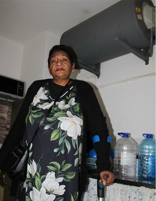 Indian woman balances on a crutch standing next to bottles of water