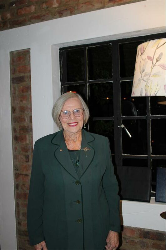 Elderly woman smiles wearing glasses and a green outfit