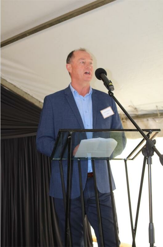 White man in a blue suit standing at a podium and talking into a microphone