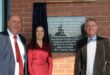 Three people, two men and a woman standing next to a plaque