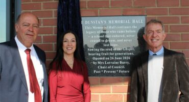 Three people, two men and a woman standing next to a plaque