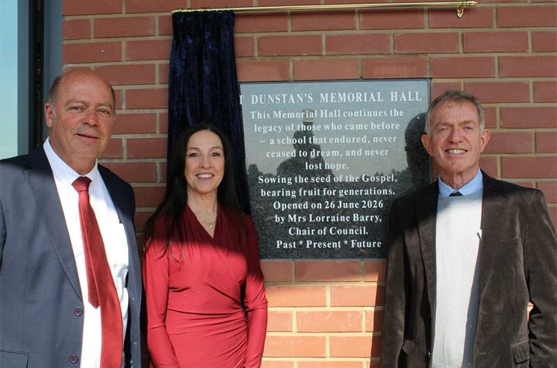 Three people, two men and a woman standing next to a plaque