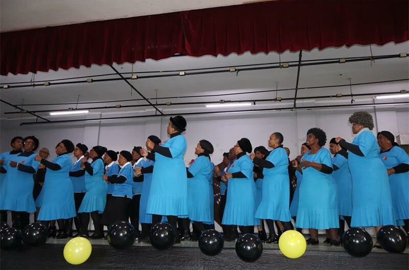 Group of black women wearing blue dresses dancing on stage