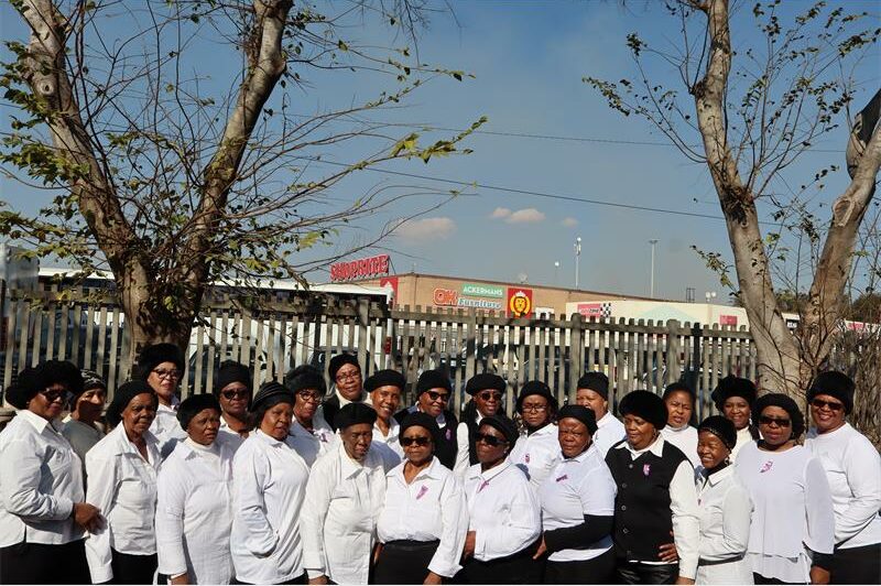 Group of black women wearing white collared shirts and black skirts smiling at the camera