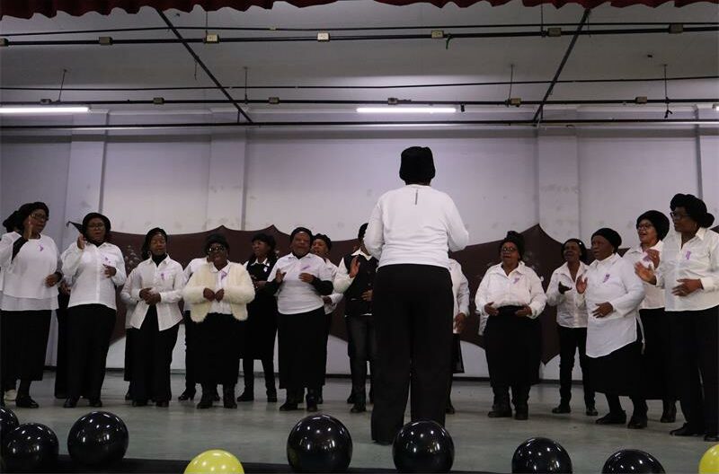 Black women wearing white shirts and black skirts singing on stage