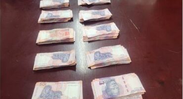 R19 500 in cash laid out in piles next to each other on a wooden table.
