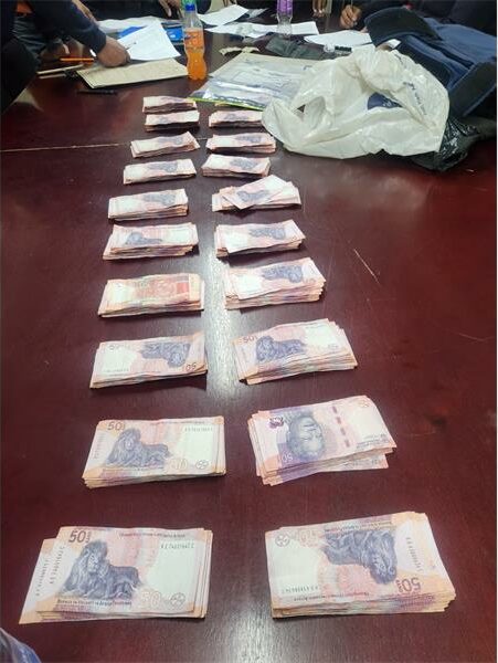 R19 500 in cash laid out in piles next to each other on a wooden table.