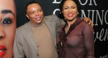 Black man wearing a suit has his hand draped over a black woman's shoulders