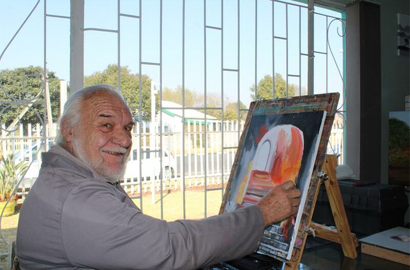 Elderly man paining in front of a window
