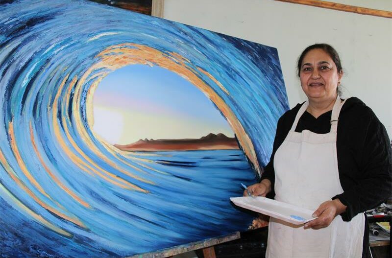 Indian woman standing in front of a paining of a crushing wave