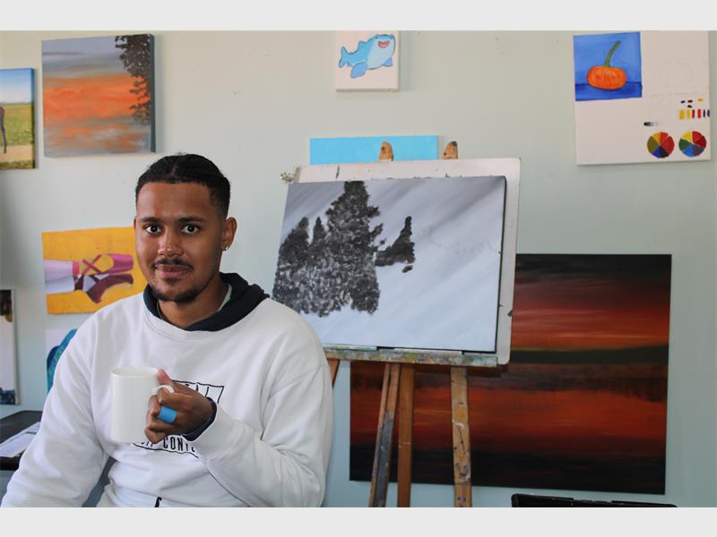 Coloured man holding a coffee mug sitting in front of an easle