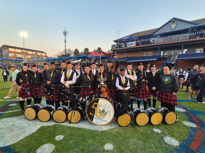 Pipe band members posing with a trophy and their instruments