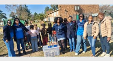 A big group of women standing next to each other with plastic containers filled with soup and party packs on top of the containers.
