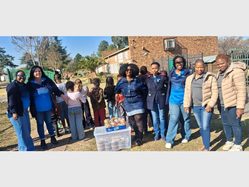 A big group of women standing next to each other with plastic containers filled with soup and party packs on top of the containers.