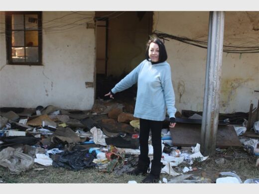a woman standing next to a pile of rubbish next to a dilapidated building