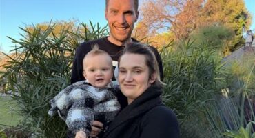 Man and woman standing in a garden holding a baby