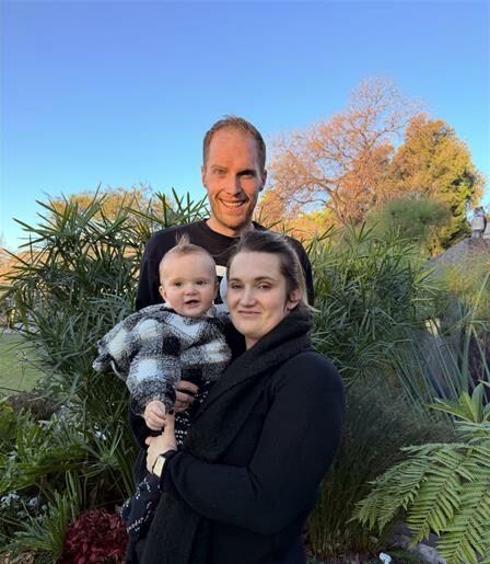 Man and woman standing in a garden holding a baby