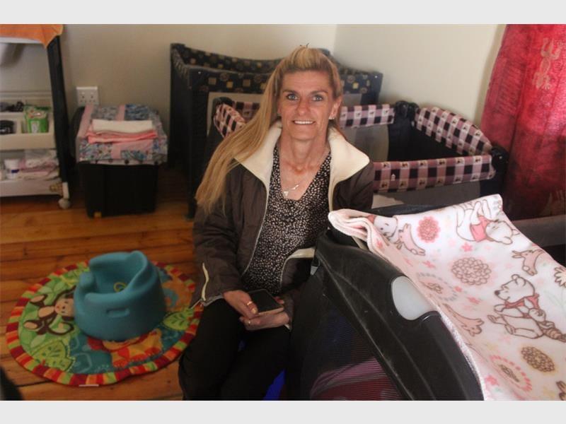 A blonde woman sitting on the floor of a nursery with camping cots in the background.
